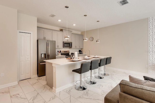 kitchen with stainless steel appliances, pendant lighting, a breakfast bar area, gray cabinets, and a kitchen island with sink