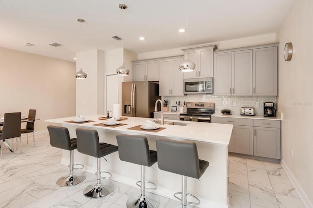 kitchen with a center island with sink, gray cabinetry, stainless steel appliances, and hanging light fixtures