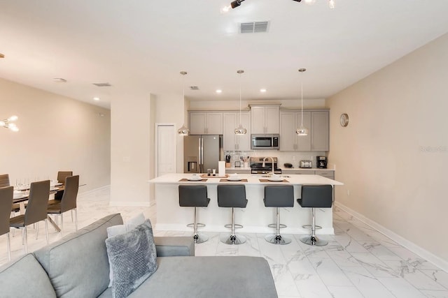 kitchen featuring a kitchen bar, gray cabinetry, stainless steel appliances, a kitchen island with sink, and decorative light fixtures