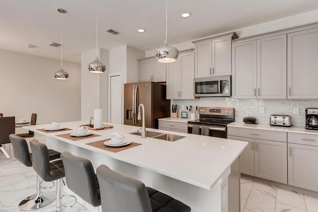 kitchen featuring sink, stainless steel appliances, decorative light fixtures, decorative backsplash, and a center island with sink