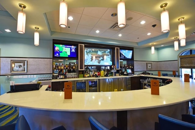 bar with a tray ceiling, a drop ceiling, and hanging light fixtures