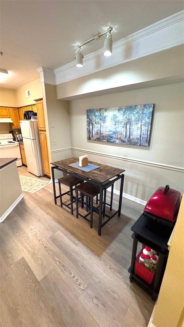 dining space with ornamental molding, light wood-type flooring, and rail lighting