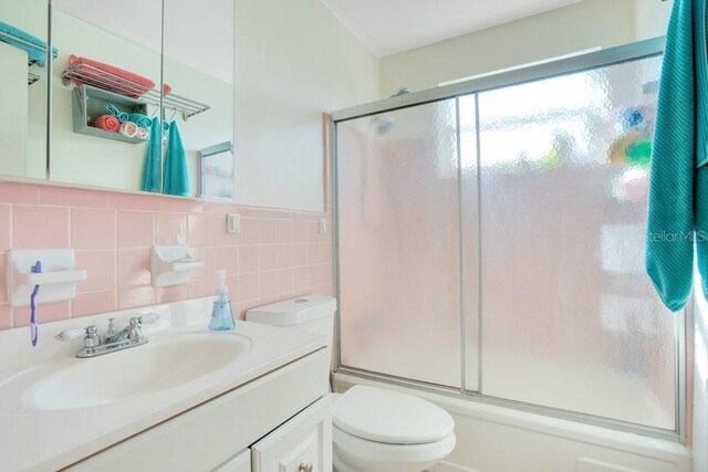full bathroom with vanity, toilet, shower / bath combination with glass door, and tile walls