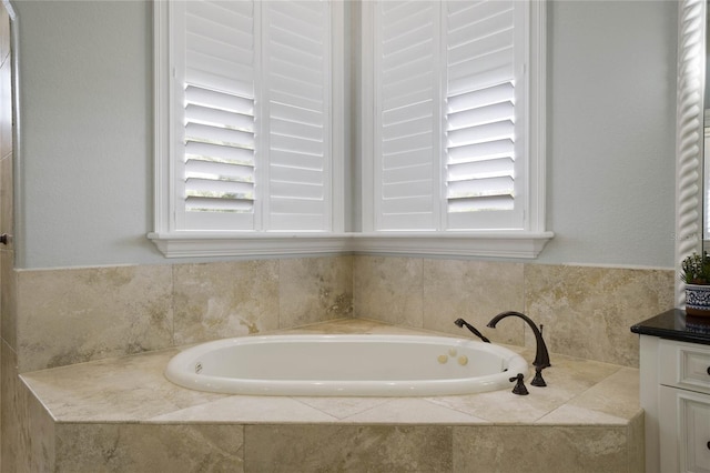 bathroom featuring tiled tub, vanity, and a healthy amount of sunlight