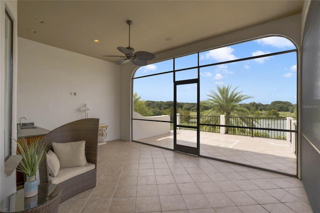 sunroom with ceiling fan, plenty of natural light, sink, and a water view