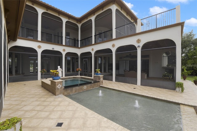 back of property with an in ground hot tub, a patio, pool water feature, and a balcony