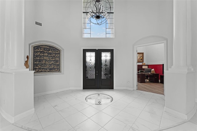 foyer featuring french doors, ornate columns, a high ceiling, and a chandelier