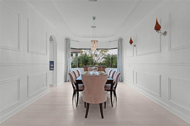 dining room featuring ornamental molding, a chandelier, light hardwood / wood-style flooring, and a tray ceiling