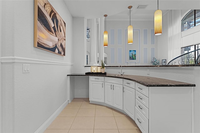 kitchen featuring white cabinets, hanging light fixtures, dark stone countertops, light tile patterned flooring, and sink