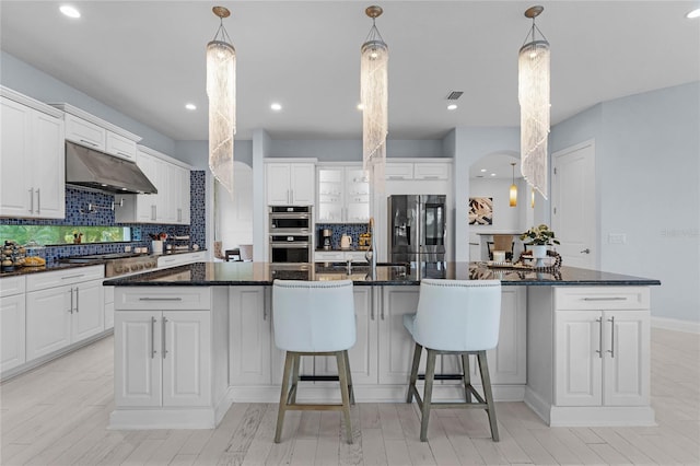 kitchen with decorative backsplash, white cabinetry, stainless steel appliances, and an island with sink