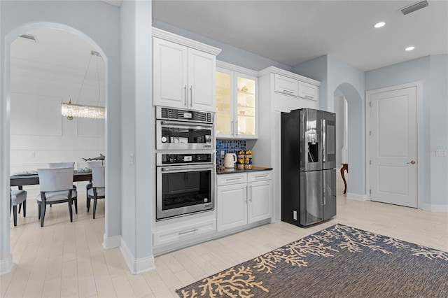 kitchen featuring white cabinets, stainless steel appliances, light wood-type flooring, and backsplash