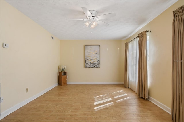 empty room featuring a textured ceiling, visible vents, light wood finished floors, a ceiling fan, and baseboards