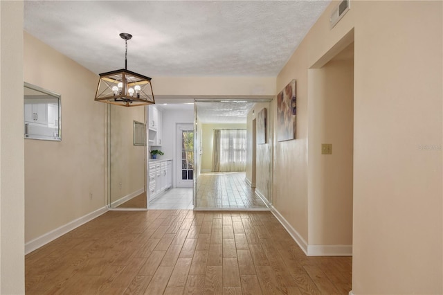 hallway with a chandelier, a textured ceiling, and light wood-type flooring