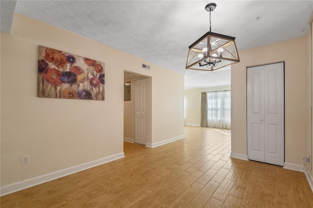 unfurnished room with a textured ceiling, baseboards, visible vents, a chandelier, and light wood-style floors