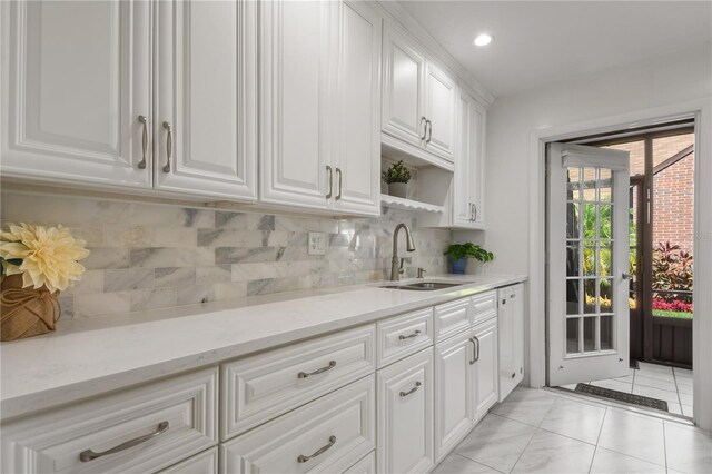 kitchen with white cabinets, backsplash, light tile patterned floors, light stone countertops, and sink