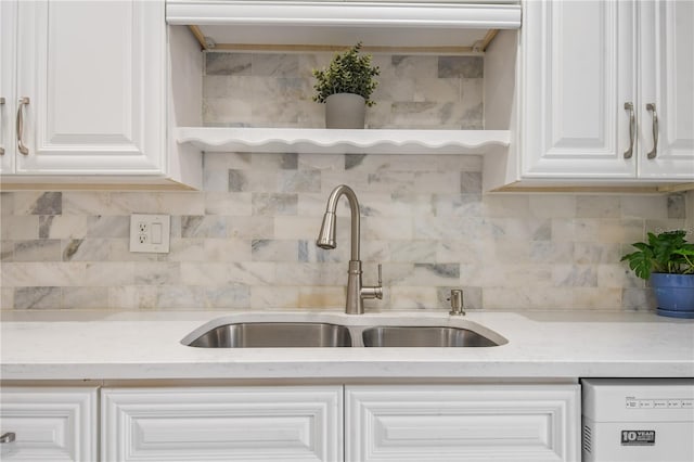 kitchen featuring white dishwasher, decorative backsplash, white cabinets, and a sink