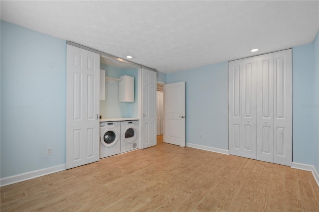 laundry area featuring washing machine and dryer, light hardwood / wood-style floors, a textured ceiling, and cabinets