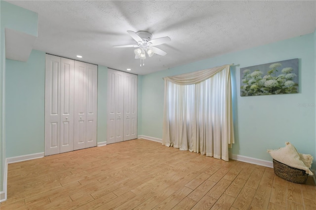 unfurnished bedroom with a textured ceiling, two closets, light wood-type flooring, and ceiling fan