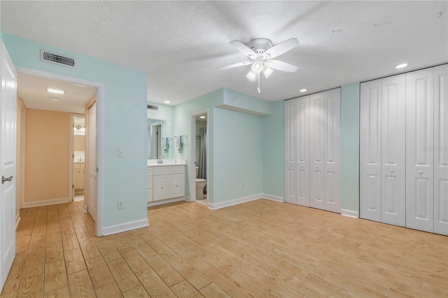 unfurnished bedroom featuring two closets, ceiling fan, a textured ceiling, connected bathroom, and light hardwood / wood-style floors