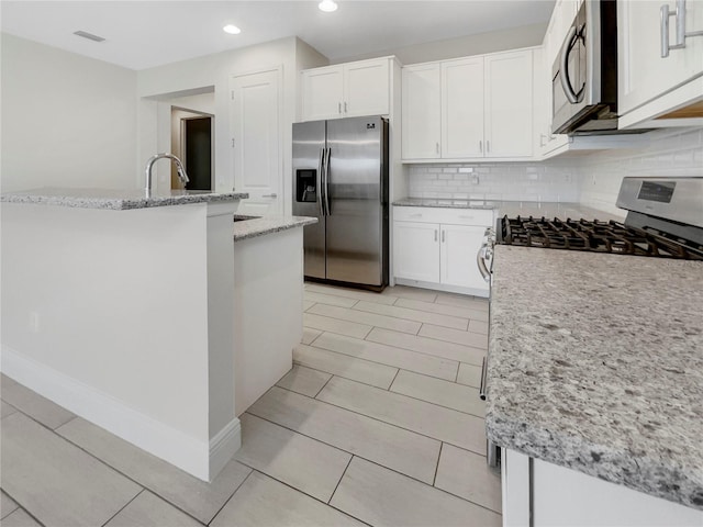 kitchen with light stone countertops, a kitchen island with sink, appliances with stainless steel finishes, and white cabinetry