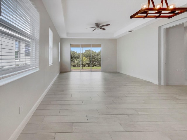 unfurnished room with ceiling fan with notable chandelier, a tray ceiling, and light hardwood / wood-style flooring