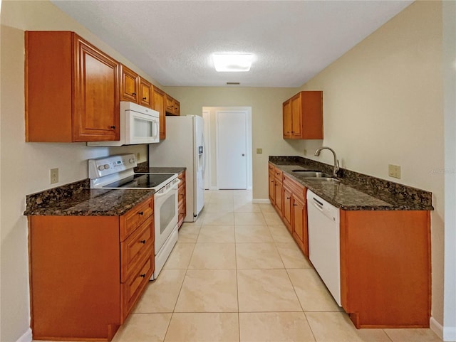 kitchen with dark stone countertops, white appliances, light tile patterned floors, a textured ceiling, and sink