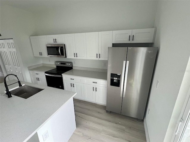 kitchen featuring white cabinets, stainless steel appliances, sink, and light hardwood / wood-style flooring