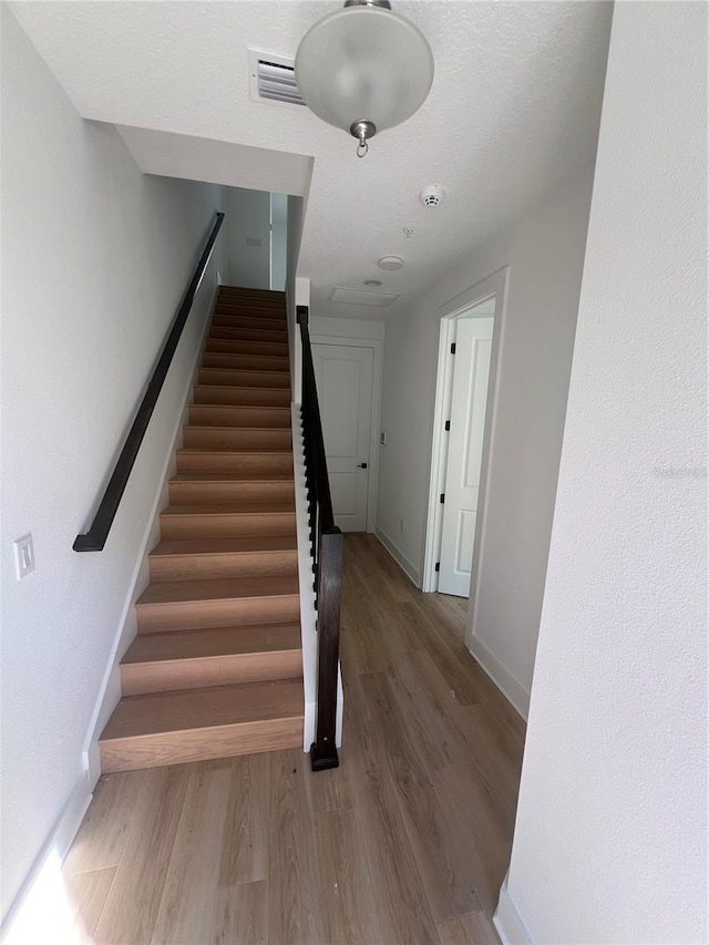 stairway with a textured ceiling and wood-type flooring