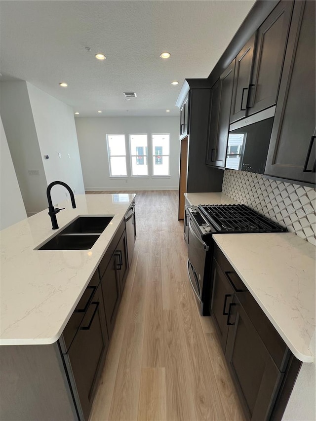 kitchen with decorative backsplash, light hardwood / wood-style floors, an island with sink, light stone countertops, and sink