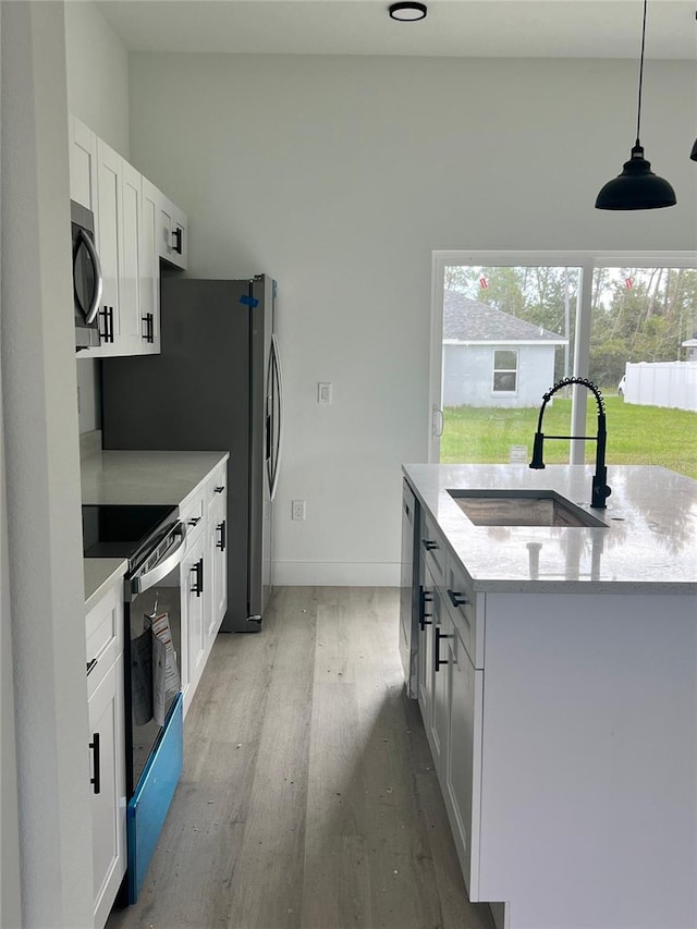 kitchen with white cabinets, sink, decorative light fixtures, appliances with stainless steel finishes, and light hardwood / wood-style floors