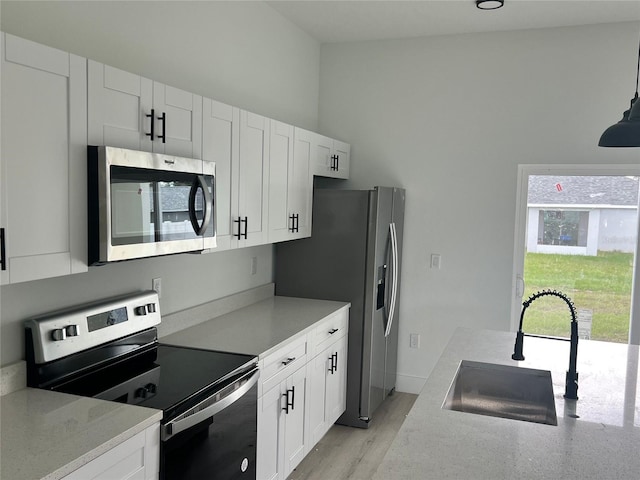 kitchen featuring appliances with stainless steel finishes, white cabinetry, sink, and vaulted ceiling