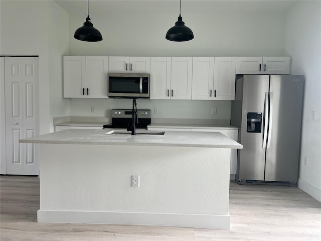 kitchen with stainless steel appliances, white cabinets, a center island with sink, and decorative light fixtures