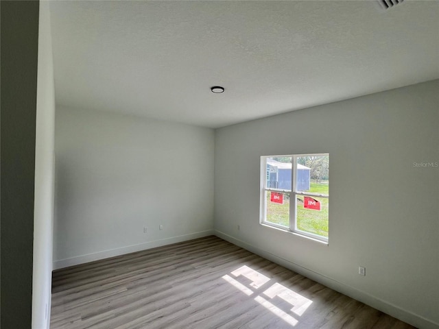 spare room featuring a textured ceiling and light hardwood / wood-style floors