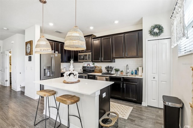 kitchen with hanging light fixtures, sink, a kitchen island, appliances with stainless steel finishes, and a breakfast bar