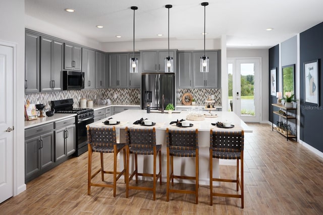 kitchen featuring appliances with stainless steel finishes, gray cabinetry, an island with sink, and hanging light fixtures