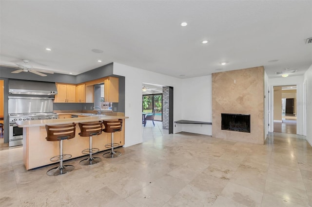 kitchen featuring wall chimney range hood, sink, kitchen peninsula, a breakfast bar area, and light brown cabinets