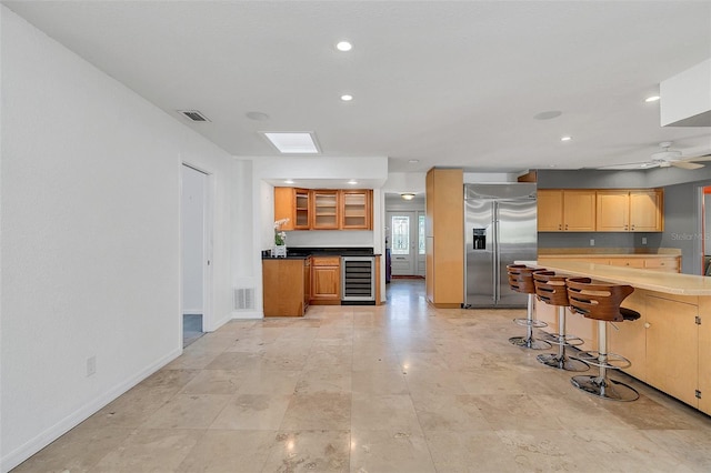 kitchen featuring a skylight, stainless steel built in refrigerator, a kitchen breakfast bar, ceiling fan, and wine cooler