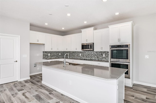 kitchen featuring light hardwood / wood-style flooring, a kitchen island with sink, stainless steel appliances, and white cabinetry