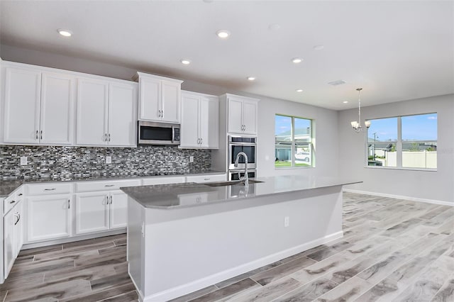 kitchen with white cabinets, an island with sink, decorative light fixtures, a chandelier, and appliances with stainless steel finishes