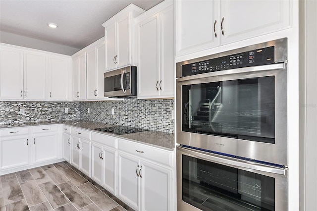 kitchen with dark stone counters, light hardwood / wood-style floors, white cabinets, decorative backsplash, and appliances with stainless steel finishes