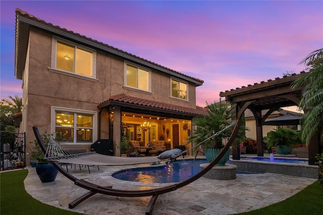 back house at dusk with a pergola, a patio, and pool water feature