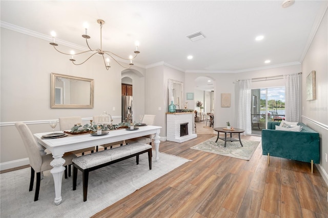 dining space with wood-type flooring, an inviting chandelier, a brick fireplace, and ornamental molding