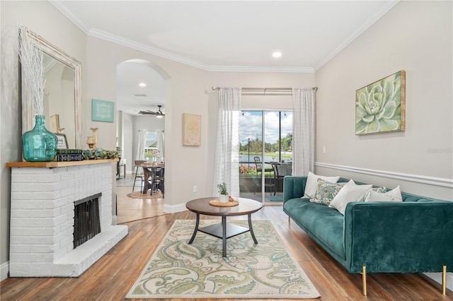 living room with ceiling fan, ornamental molding, a brick fireplace, and hardwood / wood-style floors