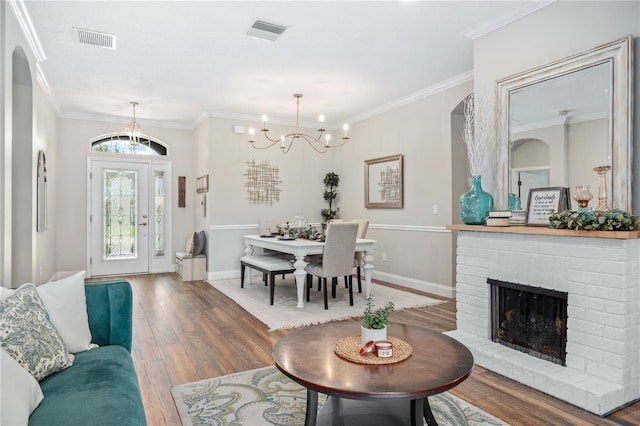 living room featuring wood-type flooring, an inviting chandelier, a fireplace, and crown molding