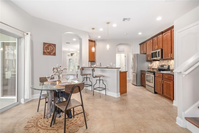 kitchen with a breakfast bar, kitchen peninsula, stainless steel appliances, backsplash, and decorative light fixtures