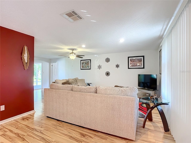 living room featuring light hardwood / wood-style flooring, a textured ceiling, and ceiling fan