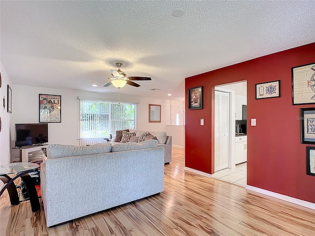 living room featuring light hardwood / wood-style floors, a textured ceiling, and ceiling fan