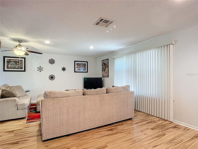 living room featuring light hardwood / wood-style flooring, a textured ceiling, and ceiling fan