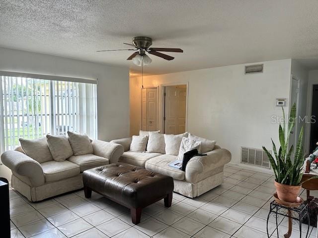 living room featuring a textured ceiling, light tile patterned flooring, and ceiling fan