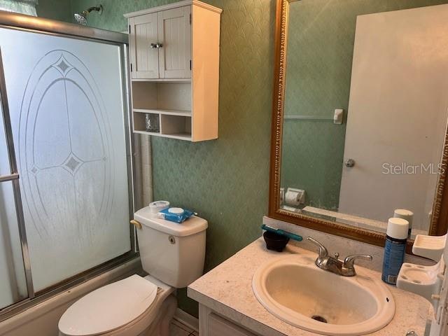 full bathroom featuring toilet, combined bath / shower with glass door, and vanity